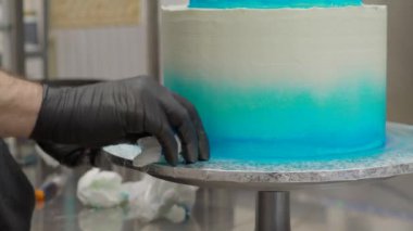 cake designer spinning smoothing and levelling frosted grandient blue white wedding cake with spatula and scraper 4k footage