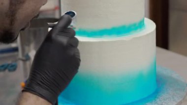 chef pastry desginer sing edible blue airbrush colour to decorate two floor layered frosted cake in blue white 4k footage