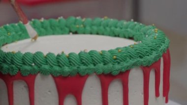 pastry chef cake designer decorating christmas red green white frosted cheesecake with piping bag 4k footage