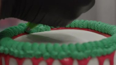 pastry chef cake designer decorating christmas red green white frosted cheesecake with piping bag 4k footage