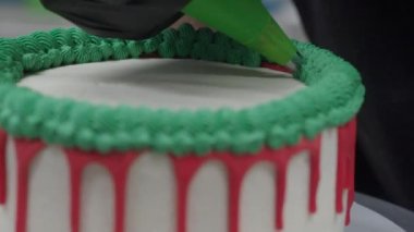 pastry chef cake designer decorating christmas red green white frosted cheesecake with piping bag 4k footage