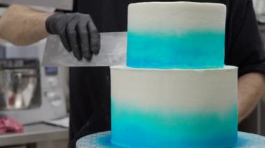 cake designer spinning smoothing and levelling frosted grandient blue white wedding cake with spatula and scraper 4k footage
