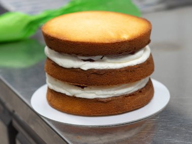 chef pastry designer confectioning a frosted 3 floor layered cake stuffed with strawberries and whipped butter cream. Cake structure before decoration.