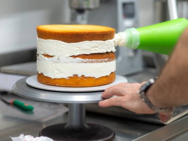 chef pastry designer confectioning a frosted 3 floor layered cake stuffed with strawberries and whipped butter cream. Cake structure before decoration.