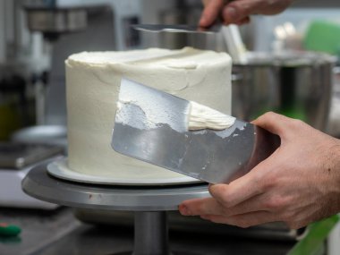 chef pastry designer confectioning a frosted 3 floor layered cake stuffed with strawberries and whipped butter cream. Cake structure before decoration.