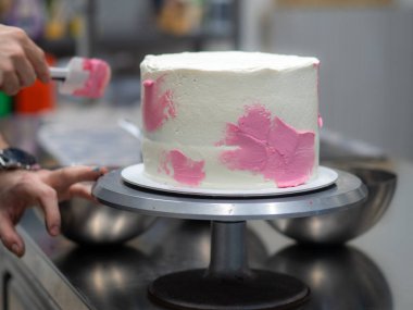 chef pastry designer confectioning a frosted 3 floor layered cake decorated with pastel creamy colors photo.