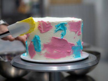 chef pastry designer confectioning a frosted 3 floor layered cake decorated with pastel creamy colors photo.