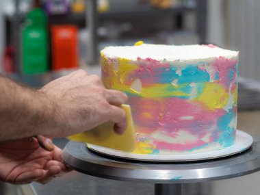 chef pastry designer confectioning a frosted 3 floor layered cake decorated with pastel creamy colors photo.