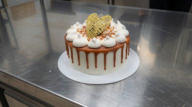 chef pastry baker finishing salty caramel frosted dripping cakes with meringues and chocolate golden heart handmade topper