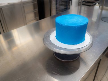 blue sprayed frosted cake on stand ready for decoration at bakery lab