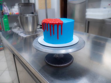 blue sprayed frosted cake on stand dripped with red ganache filling and white meringues and whipper cream on top