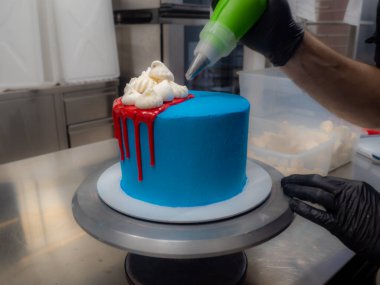 blue sprayed frosted cake on stand dripped with red ganache filling and white meringues and whipper cream on top