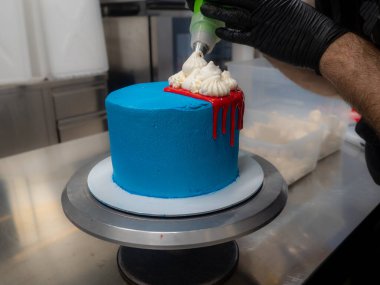 blue sprayed frosted cake on stand dripped with red ganache filling and white meringues and whipper cream on top