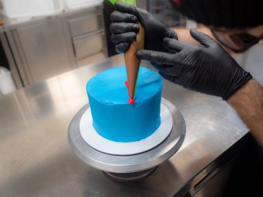 blue sprayed frosted cake on stand ready for decoration at bakery lab dripped with red