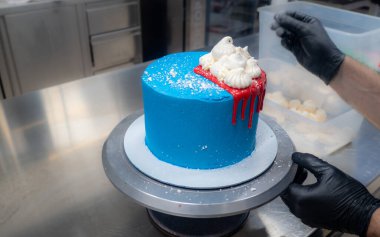 blue sprayed frosted cake on stand dripped with red ganache filling and white meringues and whipper cream on top