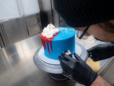 blue sprayed frosted cake on stand dripped with red ganache filling and white meringues and whipper cream on top