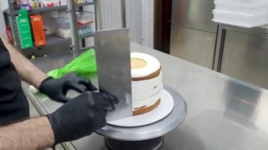 chef pastry designer confectioning a frosted 3 floor layered cake stuffed with strawberries , blueberries and whipped butter cream. Cake structure before decoration.