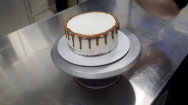 Pasta şefi tasarımcısı koyu çikolatalı kremalı beyaz pastayı kahverengimsi sıkan 4K çekimle dekore ediyor.