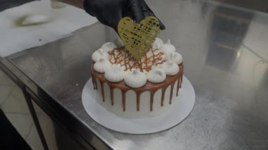 Şef hamur işi fırıncı tuzlu karamelli kremalı kekleri kremalı ve çikolata rengi altın kalpli el yapımı üstlük 4K görüntüler ile bitiriyor.