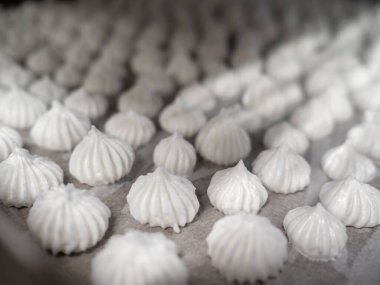 pastry chef baker artisan making white swirl and twirl meringue cones with piping bag filled with egg cream and sugar to bake for sweet preparation