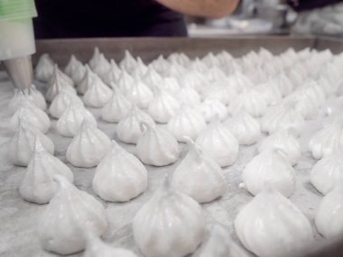 pastry chef baker artisan making white swirl and twirl meringue cones with piping bag filled with egg cream and sugar to bake for sweet preparation