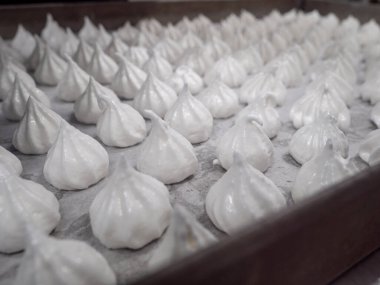 pastry chef baker artisan making white swirl and twirl meringue cones with piping bag filled with egg cream and sugar to bake for sweet preparation