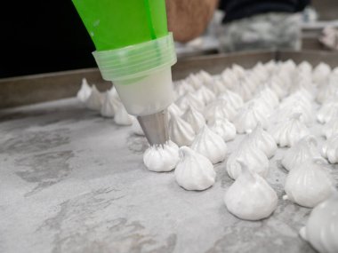 pastry chef baker artisan making white swirl and twirl meringue cones with piping bag filled with egg cream and sugar to bake for sweet preparation