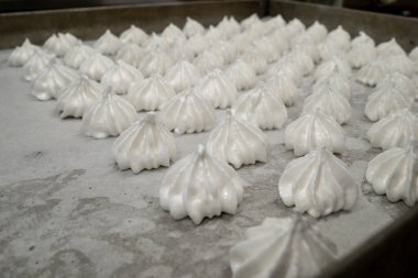 pastry chef baker artisan making white swirl and twirl meringue cones with piping bag filled with egg cream and sugar to bake for sweet preparation
