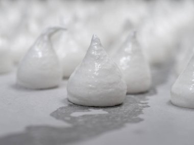 pastry chef baker artisan making white swirl and twirl meringue cones with piping bag filled with egg cream and sugar to bake for sweet preparation
