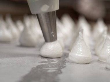pastry chef baker artisan making white swirl and twirl meringue cones with piping bag filled with egg cream and sugar to bake for sweet preparation