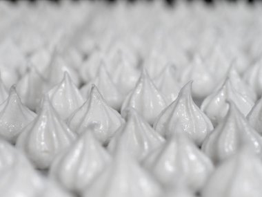 pastry chef baker artisan making white swirl and twirl meringue cones with piping bag filled with egg cream and sugar to bake for sweet preparation