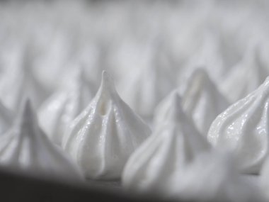 pastry chef baker artisan making white swirl and twirl meringue cones with piping bag filled with egg cream and sugar to bake for sweet preparation