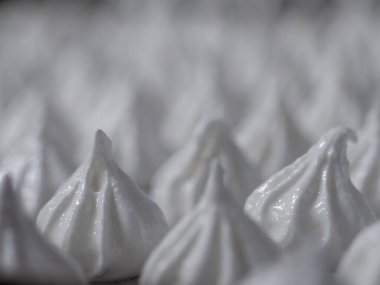 pastry chef baker artisan making white swirl and twirl meringue cones with piping bag filled with egg cream and sugar to bake for sweet preparation