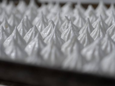 pastry chef baker artisan making white swirl and twirl meringue cones with piping bag filled with egg cream and sugar to bake for sweet preparation