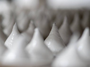 pastry chef baker artisan making white swirl and twirl meringue cones with piping bag filled with egg cream and sugar to bake for sweet preparation