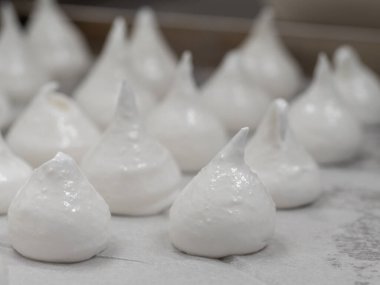 pastry chef baker artisan making white swirl and twirl meringue cones with piping bag filled with egg cream and sugar to bake for sweet preparation