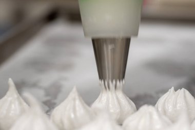 pastry chef baker artisan making white swirl and twirl meringue cones with piping bag filled with egg cream and sugar to bake for sweet preparation