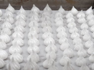 pastry chef baker artisan making white swirl and twirl meringue cones with piping bag filled with egg cream and sugar to bake for sweet preparation