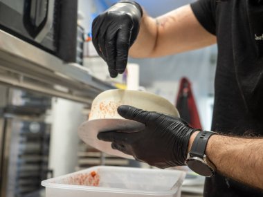 Pasta tasarımcısı beyaz kremalı pastaya kırmızı şeker serpiyor.