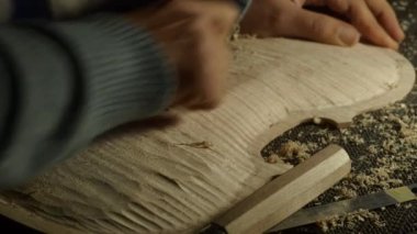 Keman ustası zanaatkar, 4k çekimlerindeki atölyedeki tezgahta yontulmuş çiğ akçaağaç ahşap keman oyma masası yontuyor.
