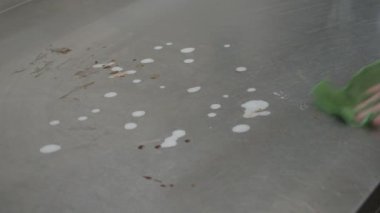 Bir restoranda deterjan ve mikrofiber bezle yemek pişirdikten sonra kirli profesyonel mutfak tezgahını temizleyen personel.