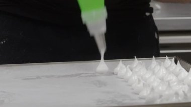 Pasta şefi fırıncı beyaz girdap yapıyor ve krema ve şeker dolu boru torbasıyla kremalı krema ve krema çeviriyor.