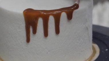Hamur işi aşçısı güve beyazı kremalı keki bitiriyor. Karamel şurubu damlıyor ve el yapımı kremalar. 4K görüntüler.