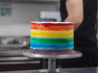 Pasta şefi düğün partisi için lgbt gökkuşağı renginde buzlu kek üzerinde çalışıyor. Doğum günü pastası. Gökkuşağı kağıt bardak kağıtları. Doğum günün kutlu olsun. Tatilleri kutluyoruz. LGBT gururu.