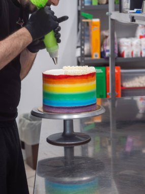 Pasta şefi düğün partisi için lgbt gökkuşağı renginde buzlu kek üzerinde çalışıyor. Doğum günü pastası. Gökkuşağı kağıt bardak kağıtları. Doğum günün kutlu olsun. Tatilleri kutluyoruz. LGBT gururu.