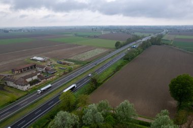 Piacenza, İtalya - Nisan 2023 Kargo kamyonları ve otoyoldaki araçlar a1 otostrada del sole hava manzaralı Padain düz kırsal alanları arasında