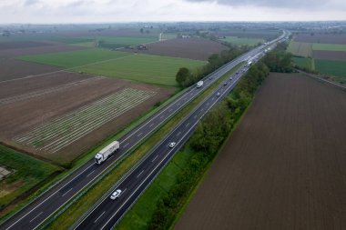Piacenza, İtalya - Nisan 2023 Kargo kamyonları ve otoyoldaki araçlar a1 otostrada del sole hava manzaralı Padain düz kırsal alanları arasında