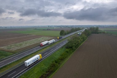Piacenza, İtalya - Nisan 2023 Kargo kamyonları ve otoyoldaki araçlar a1 otostrada del sole hava manzaralı Padain düz kırsal alanları arasında
