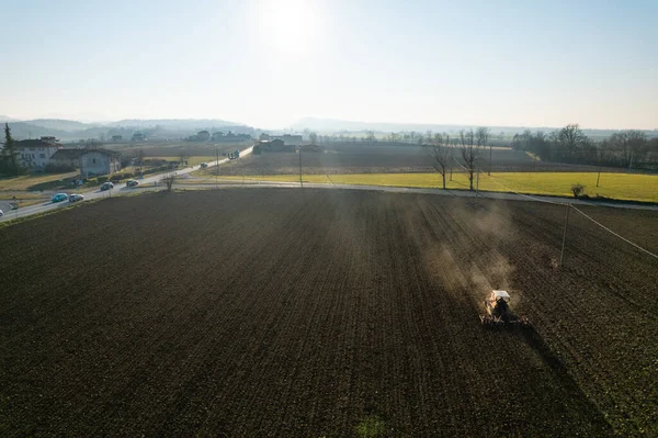 farmer driving a crawler tractor drags a cloud of dust behind, ploughing, power harrowing surface crust breaking to facilitate the birth and seeding of plants on dry soil