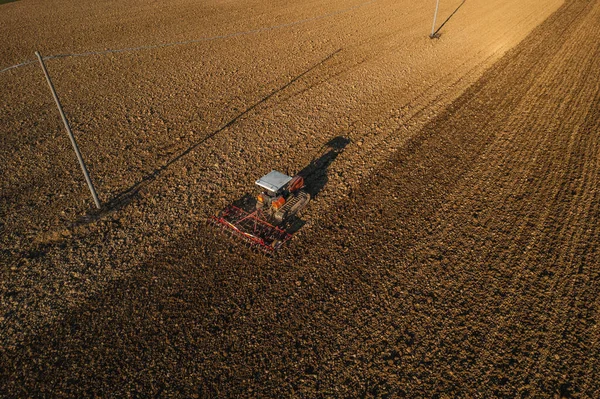 farmer driving a crawler tractor drags a cloud of dust behind, ploughing, power harrowing surface crust breaking to facilitate the birth and seeding of plants on dry soil